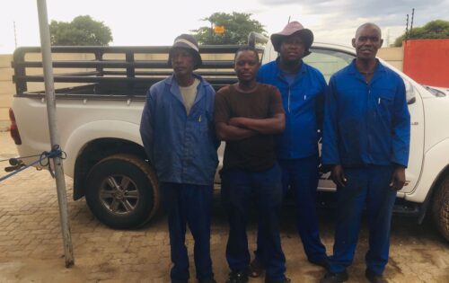 Four Scrap Salvage workers stand in front of a white pickup truck.